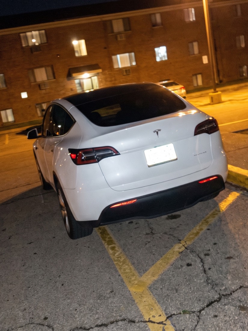 A white SUV parked at night across the yellow hatched stripes of a fire lane in an apartment complex parking lot